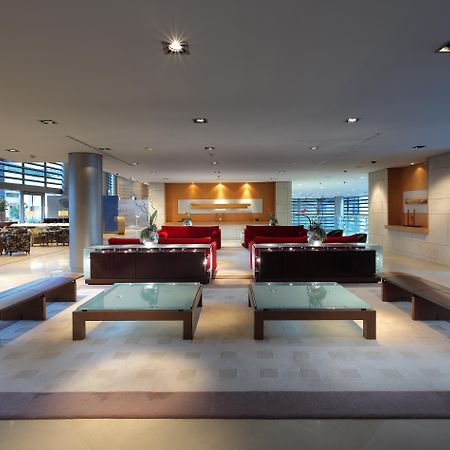 Eurostars Grand Marina Hotel Gl Barcelona Ngoại thất bức ảnh The photo shows a modern and spacious interior, likely of a lobby or waiting area. It features several red sofas arranged in a conversational layout, complemented by glass-top coffee tables. The lighting is bright and there are large windows, allowin