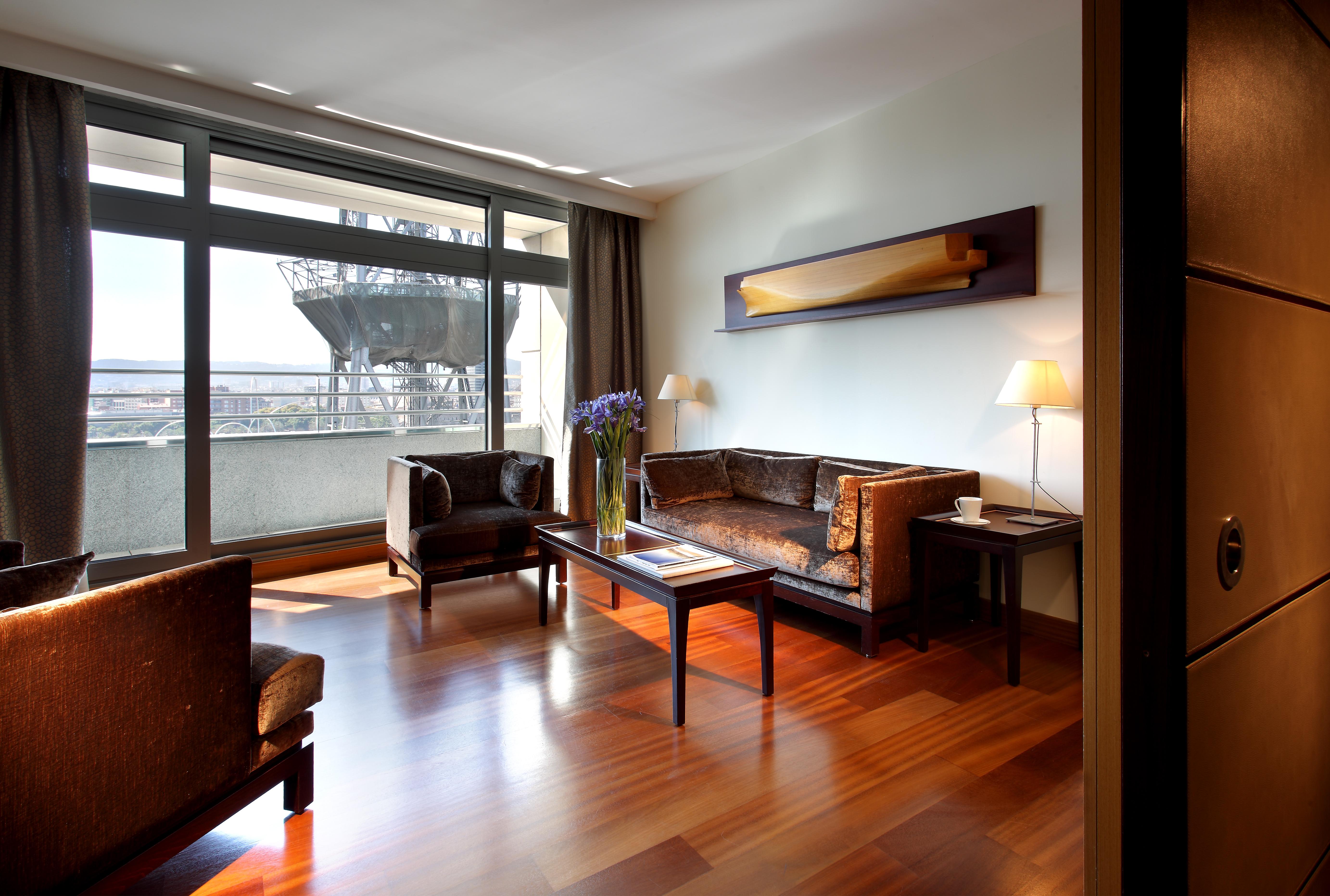 Eurostars Grand Marina Hotel Gl Barcelona Ngoại thất bức ảnh The photo depicts a modern living room setting. It features a spacious area with large windows allowing natural light to flood in. The room is furnished with two dark chairs and a brown couch, all arranged around a wooden coffee table. A decorative l