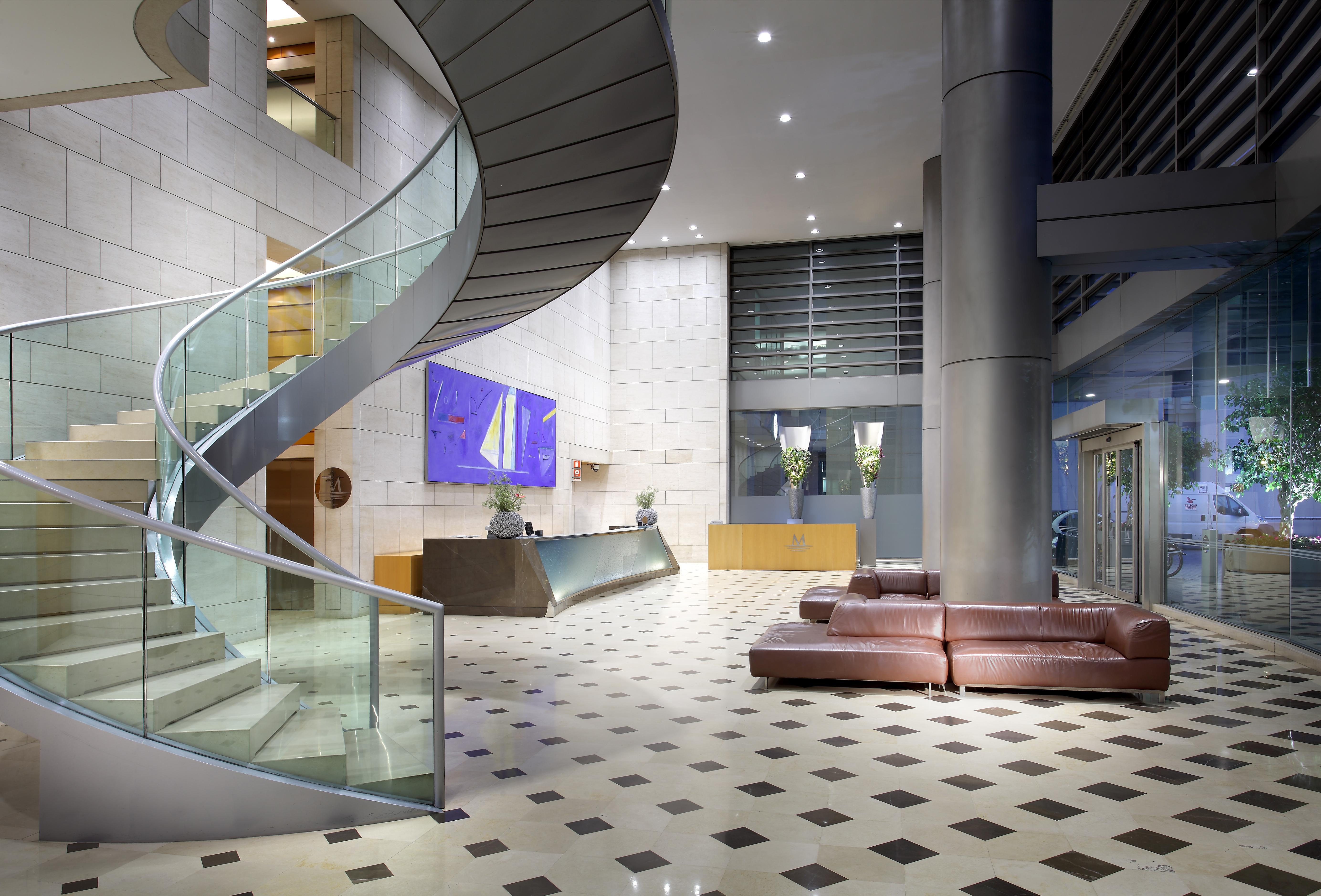 Eurostars Grand Marina Hotel Gl Barcelona Ngoại thất bức ảnh The photo shows a modern hotel or office lobby featuring a sleek, spiral staircase made of glass and metal. The staircase is accompanied by a large, open space with a tiled floor that has a checkered pattern, combining light and dark tiles. 

To the 