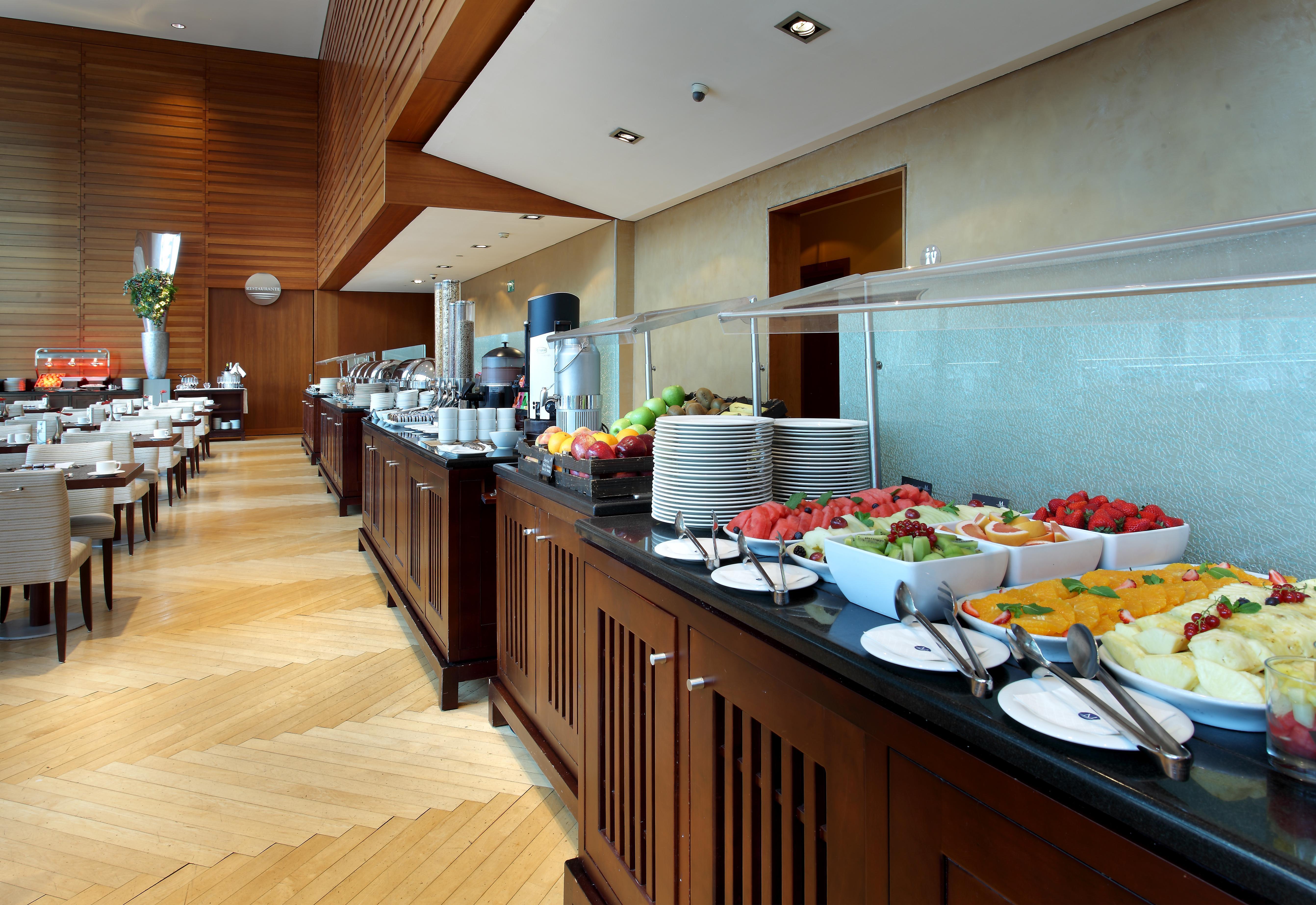 Eurostars Grand Marina Hotel Gl Barcelona Ngoại thất bức ảnh The photo shows a well-organized buffet setup in a modern dining area. There is a long counter made of wood, displaying a variety of food items. Several bowls filled with fresh fruits, such as melons and strawberries, are prominently placed. In the b