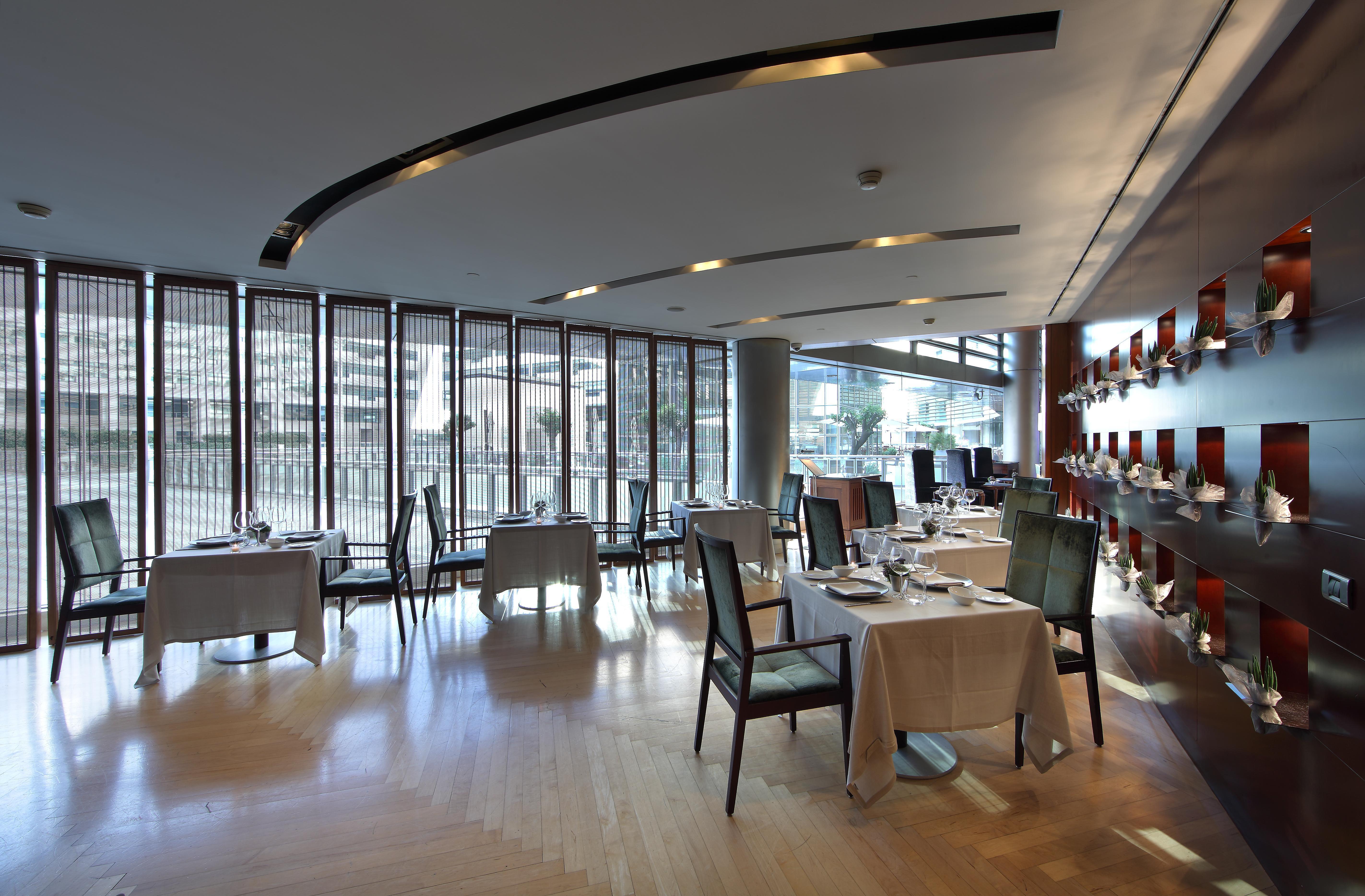 Eurostars Grand Marina Hotel Gl Barcelona Ngoại thất bức ảnh The photo shows a modern and elegant restaurant interior. There are several dining tables, each covered with tablecloths and set with cutlery. The restaurant features large windows that allow natural light to illuminate the space, creating a warm atm