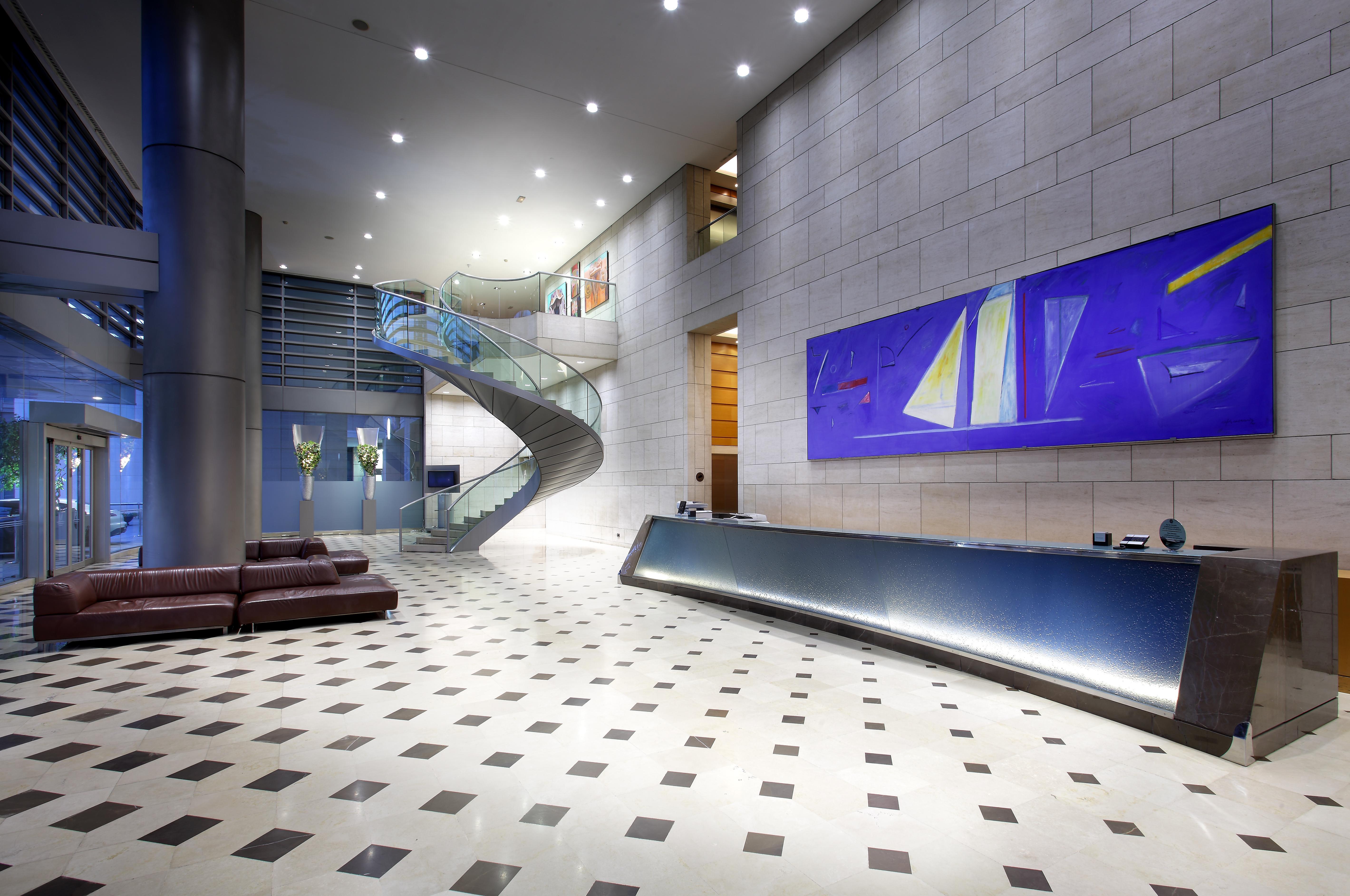 Eurostars Grand Marina Hotel Gl Barcelona Ngoại thất bức ảnh The photo shows a modern lobby or reception area. There is a sleek reception desk along one wall, featuring a polished surface. To the left, a spacious staircase with a glass guardrail leading to an upper level can be seen, framed by walls decorated 