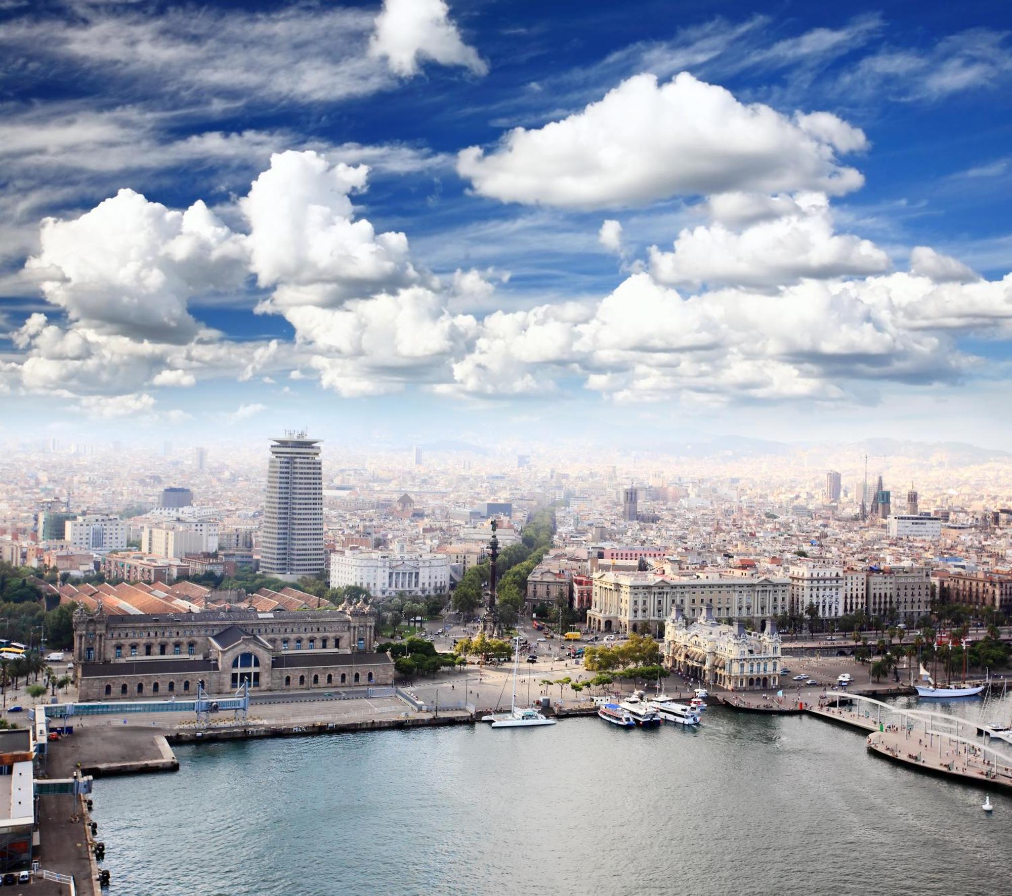 Eurostars Grand Marina Hotel Gl Barcelona Ngoại thất bức ảnh The image shows a panoramic view of a cityscape, likely featuring a coastal area with a harbor. In the foreground, there are buildings near the water, including a large structure that might be a historic or notable building. The scene extends into th
