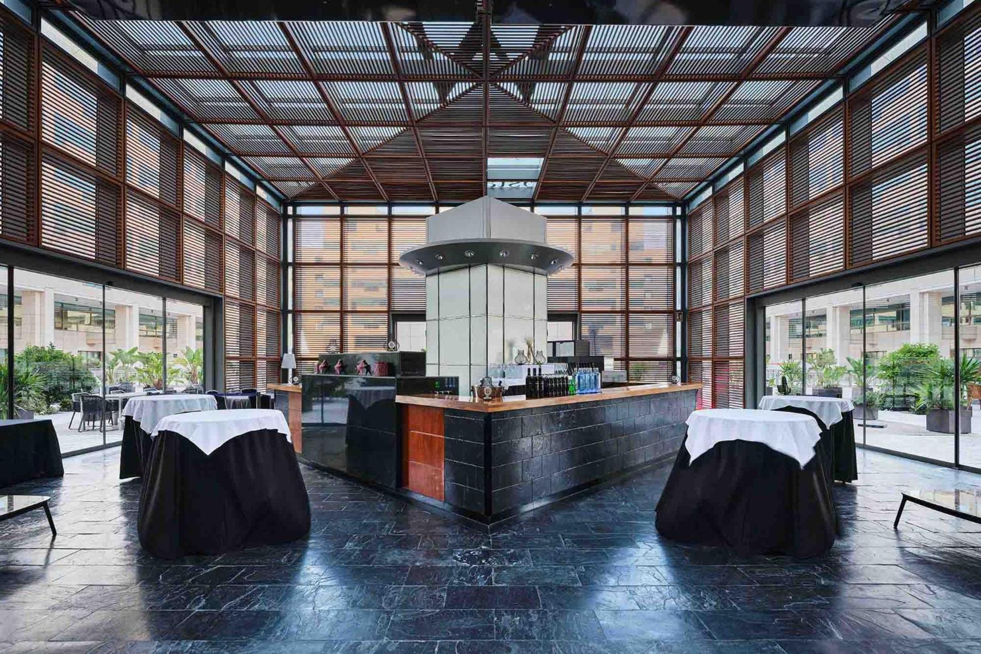 Eurostars Grand Marina Hotel Gl Barcelona Ngoại thất bức ảnh The photo shows the interior of a modern restaurant featuring a sleek bar area. The bar is centrally located and has a metallic structure with a contemporary design. Surrounding the bar are several tables covered with dark cloths and white table runn