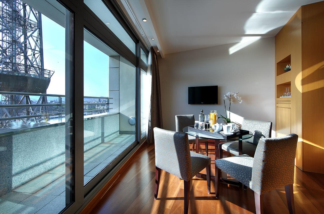 Eurostars Grand Marina Hotel Gl Barcelona Ngoại thất bức ảnh The photo shows a modern and bright room that features large windows with panoramic views. Inside, there is a circular dining table surrounded by upholstered chairs. On the table, there are items that suggest a meal or refreshments, such as drinks an