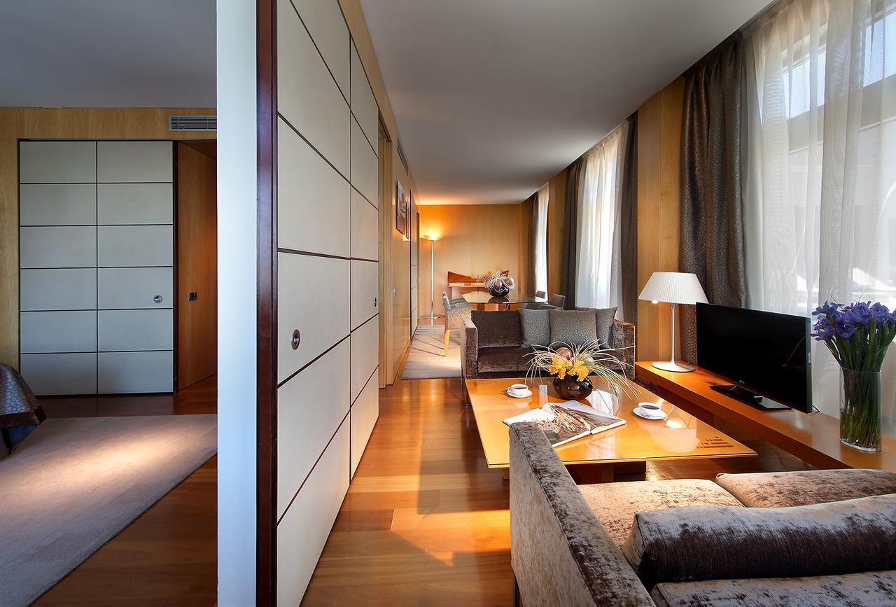 Eurostars Grand Marina Hotel Gl Barcelona Ngoại thất bức ảnh The photo shows a modern, well-lit interior space, likely a living room or suite. On one side, there are large windows letting in natural light, and the walls are adorned with soft colors. A comfortable seating area features a plush sofa and chairs, 